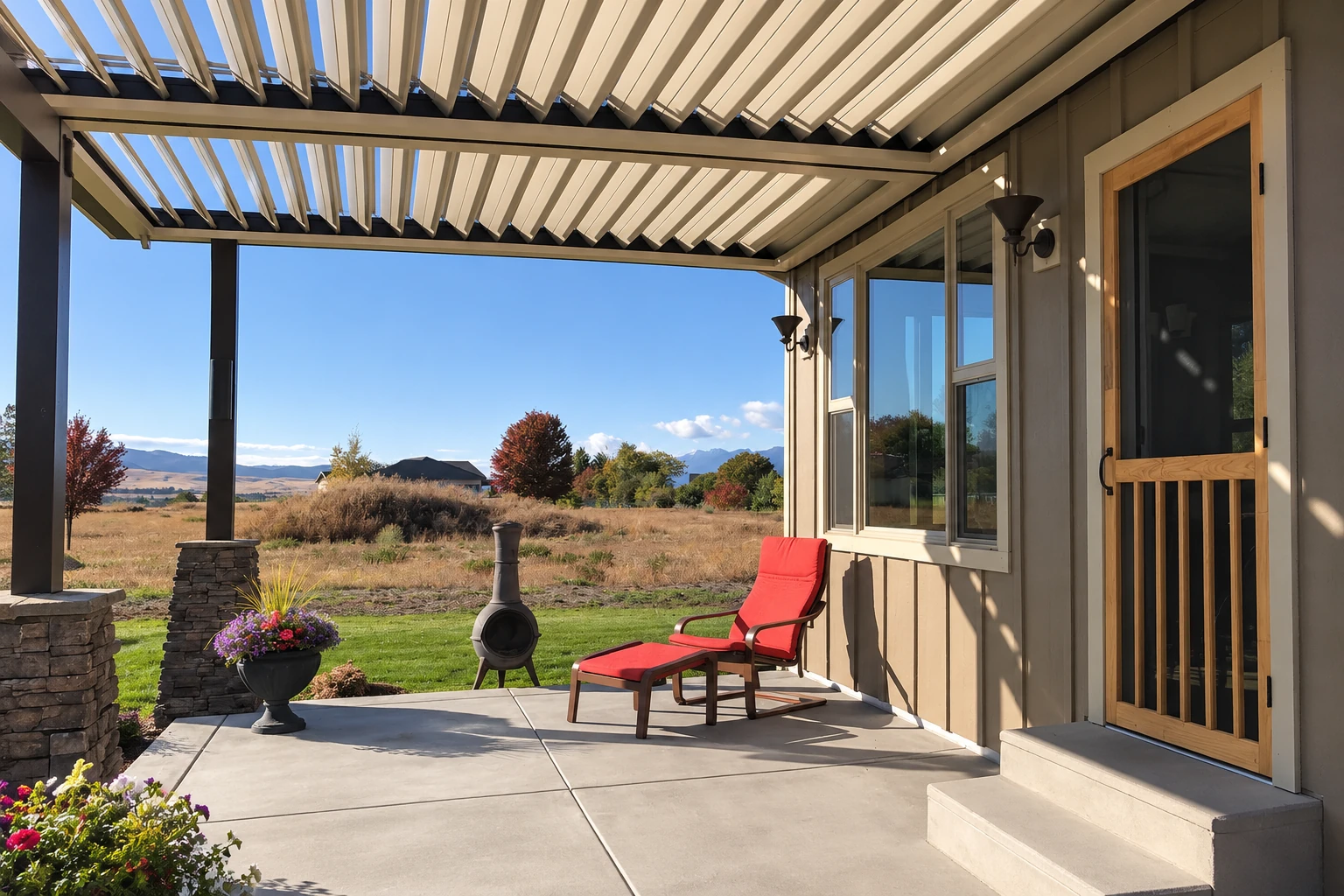 A smooth concrete patio sits beneath a slatted pergola beside a house, furnished with a red lounge chair and a freestanding stove.