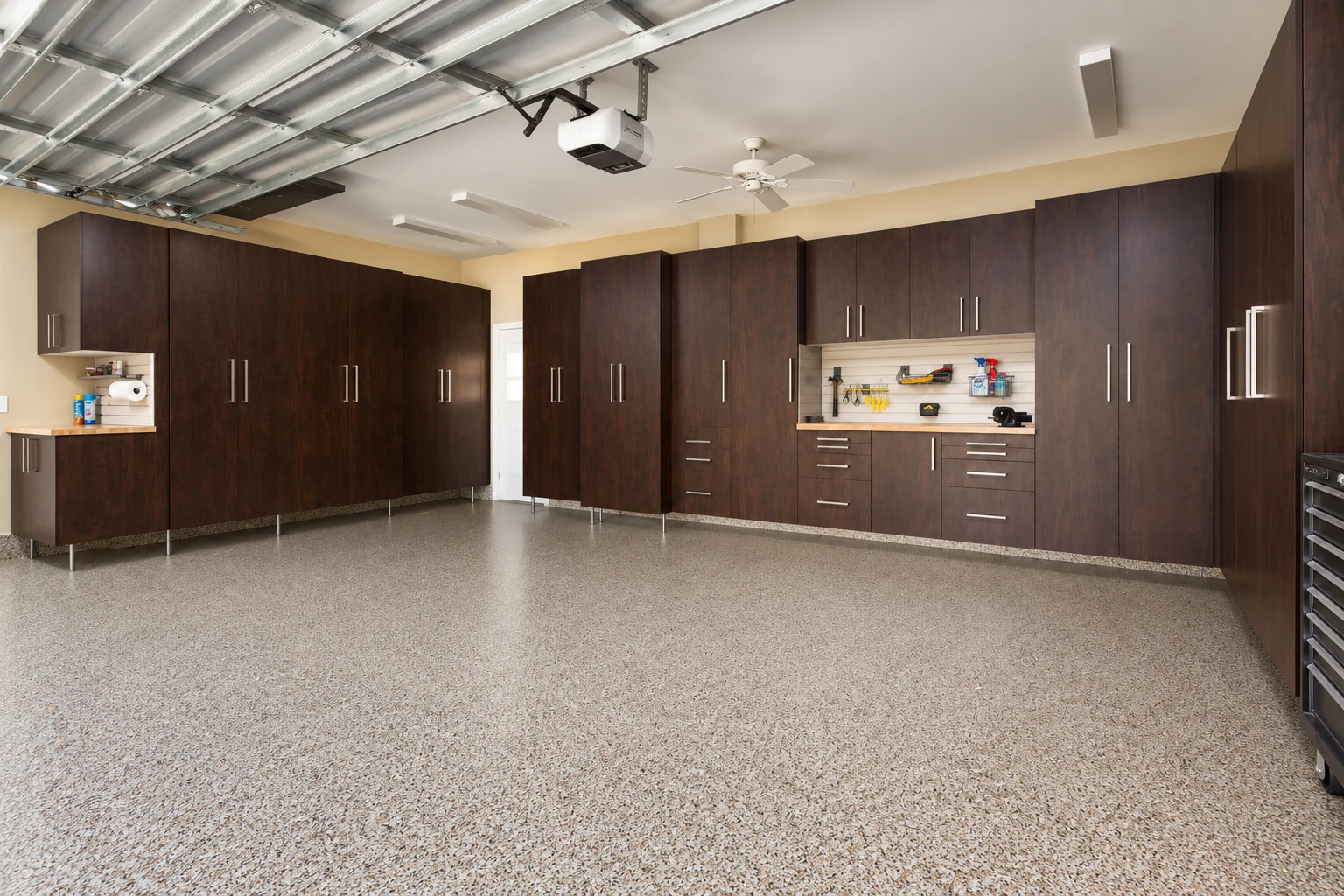A speckled concrete garage floor beneath dark wood cabinets and a wall-mounted tool area.